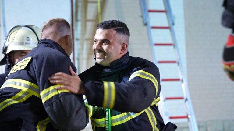 Ein Feuerwehrmann schüttelt einem anderen Feuerwehrmann lächelnd die Hand.