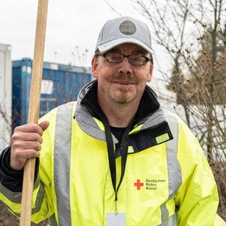 Mann in Neongelber Arbeitsweste mit Besen in der Hand