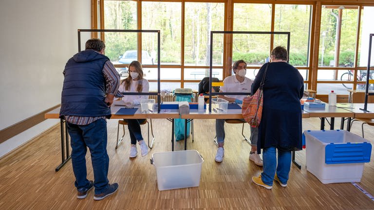 Eine junge Frau und ein junger Mann hinter Plexiglas im Schnelltestzentrum