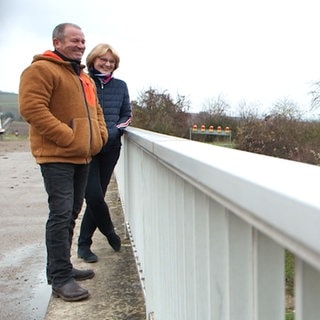 Elke und Thomas schauen von einem Brückengeländer auf die Straße und lächeln