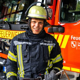 Junger Mann in Feuerwehrmontur vor einem Feuerwehrauto der Mainzer Berufsfeuerwehr