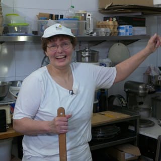 Frau mit Brille, kurzen Haaren und weißer Mütze und T-Shirt steht am Ofen in der Bäckerei