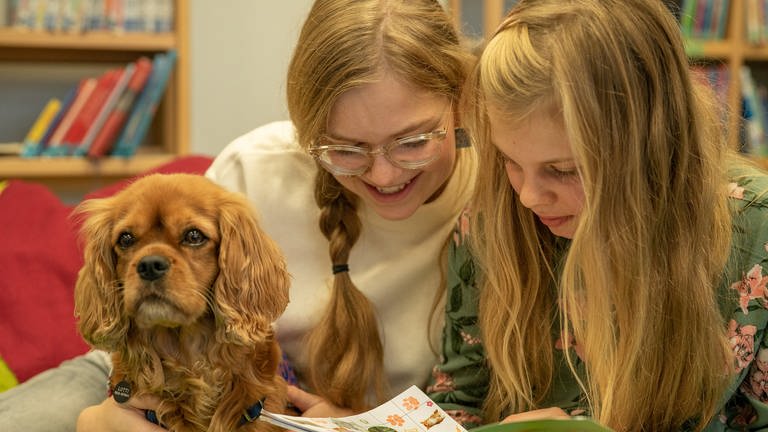 Sophie mit einer Schülerin und Hund Lotti beim Lesen eines Buches.