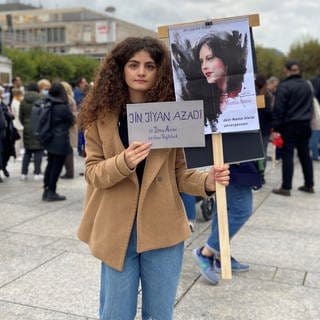 Eine junge Frau hält in Mainz bei einer Demo für Freiheit im Iran zwei Schilder in den Händen.