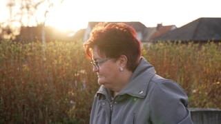 Ältere Frau mit roten Haaren vor Feld im Sonnenuntergang