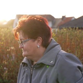 Ältere Frau mit roten Haaren vor Feld im Sonnenuntergang