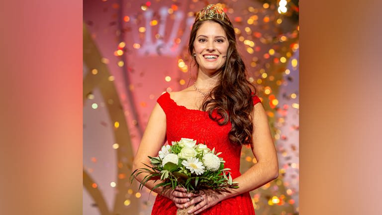 Junge Frau im roten Kleid mit Krone und Blumenstrauß, im Hintergrund Konfetti.