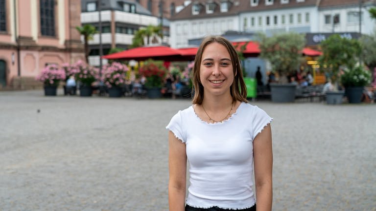 Eine junge Frau steht auf dem Wormser Marktplatz und lächelt in die Kamera.