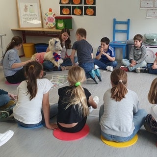 Kinder sitzen in einem Kreis auf dem Boden.