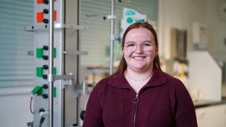 Junge Frau mit Brille in rotem Pullover lächelt in Kamera.