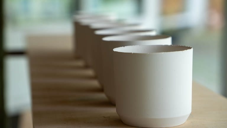 Mehrere selbstgemachte Tassen in weiß stehen in einem Regal.