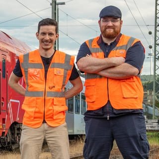 Zwei junge Männer mit Warnwesten posieren vor einer Lok