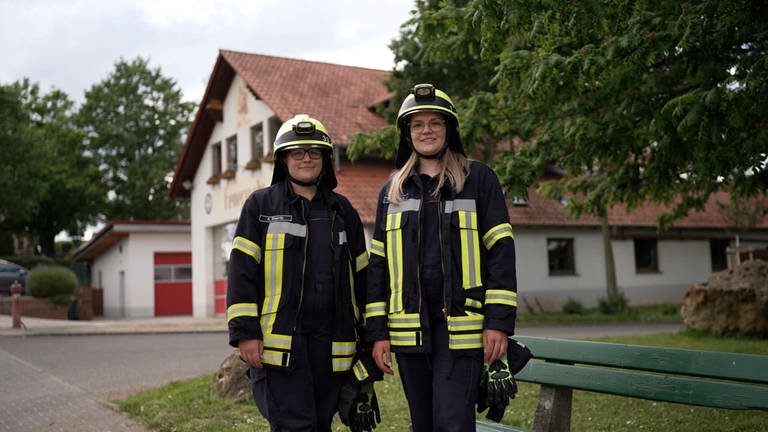 Die zwei Schwestern stehen nebeneinander und tragen einen Feuerwehranzug. 