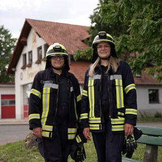 Die zwei Schwestern stehen nebeneinander und tragen einen Feuerwehranzug. 