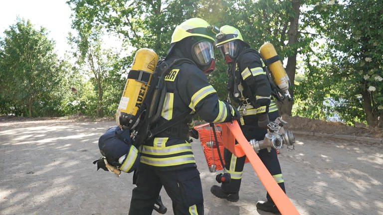 Zwei Feuerwehrmenschen haben einen Schlauch in der Hand.