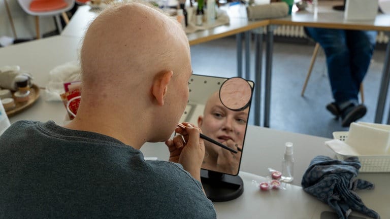 Eine Frau mit wenigen Haaren schminkt sich in einem Spiegel die Lippen.