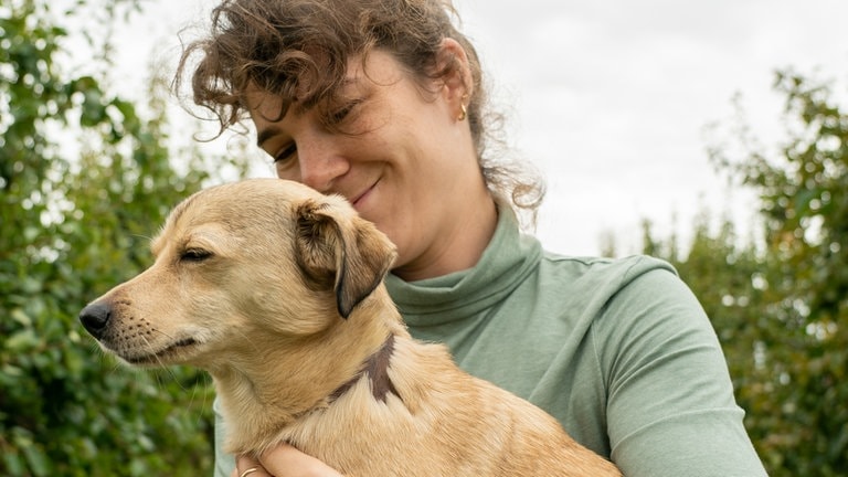 Junge Frau hält kleinen Hund mit Narben und kahlen Stellen ohne Fell.