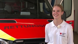 Eine Junge Frau mit DRK-T-Shirt steht vor einem Rettungswagen. Jette macht mit 17 neben der Schule eine Ausbildung zur Rettungssanitäterin.