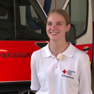 Eine Junge Frau mit DRK-T-Shirt steht vor einem Rettungswagen. Jette macht mit 17 neben der Schule eine Ausbildung zur Rettungssanitäterin.