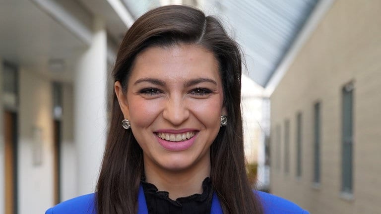 Junge Frau mit braunen Haaren und blauem Blazer lächelt in die Kamera.