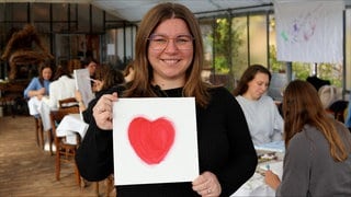 Eine junge Frau hält eine Leinwand mit einem großen roten Herz in der Hand.