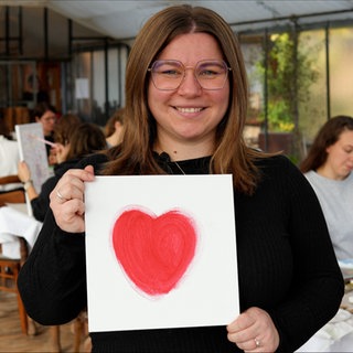 Eine junge Frau hält eine Leinwand mit einem großen roten Herz in der Hand.