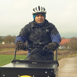 Mann fährt mit Lastenbike übers Feld