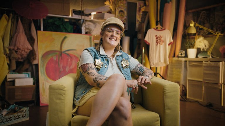 Influencerin Kim Hoss, vom Podcast „The Sirens Collective”, sitzt auf einem Sofa und lächelt in die Kamera.
