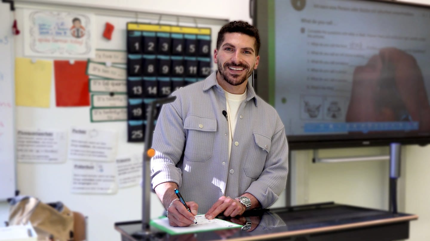Resul ist Lehrer an einer Realschule in Schorndorf. Er steht vor der Tafel und lächelt in die Kamera.