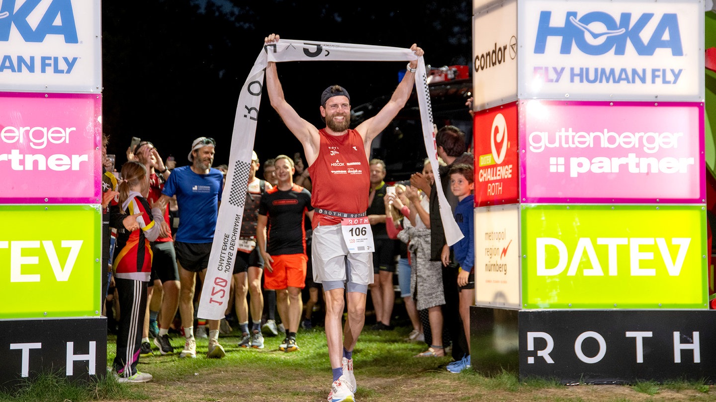 Jonas Deichmann ist im Ziel eingelaufen. Er hält das Zielband nach seinem Weltrekord von 120 Triathlons auf Langdistanz am Stück.