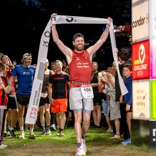 Jonas Deichmann ist im Ziel eingelaufen. Er hält das Zielband nach seinem Weltrekord von 120 Triathlons auf Langdistanz am Stück.