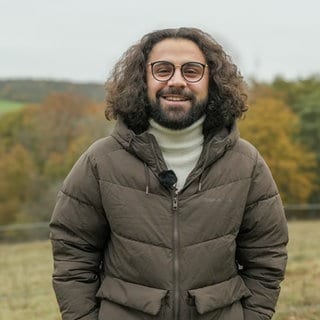 Ali auf einer seiner liebsten Spazierstrecken mit Blick auf den Fernsehturm in Stuttgart, er lächelt in die Kamera.