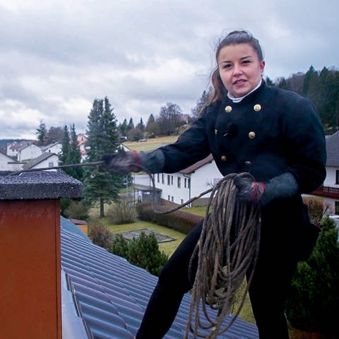 Schornsteinfegerin Janina steht auf einem Dach und reinigt den Schornstein.