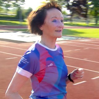 Karin ist 81 Jahre, joggt in Sportklamotten auf einem Sportplatz und gibt ein Lauftraining für Anfänger