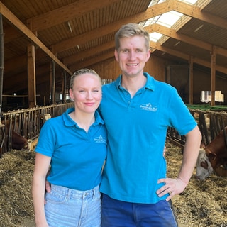 Felix und Sarah Schwenk betreiben den Benzinger Hof in 8. Generation. Sie stehen Arm in Arm im Kuhstall. Sie lachen in die Kamera und erzählen von ihrem Arbeitsalltag.