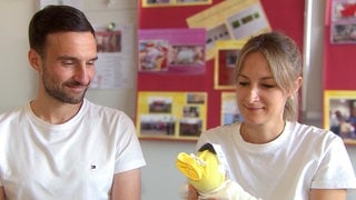 Ines und Marcel sind Eltern von einem Frühchen. Sie üben den Umgang mit ihrem Kind an einer Puppe. 