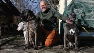 Hundetrainer Michael setzt sich für die Rehabilitation von Hunden ein. Er kniet auf den Boden und hält drei Hunde an ihren Halsbändern fest. Er lacht in die Kamera.