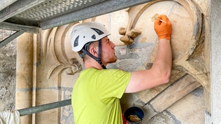  Jannis mach sein FSJ in der Denkmalpflege auf dem Ulmer Münster. Er ist zu einer Wand gedreht und bearbeitet einen Stein. Er trägt einen Helm und ein grünes T-Shirt.