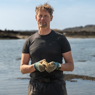 Lars ist Austernfarmer auf einer schottischen Insel und hält eine Auster in der Hand.