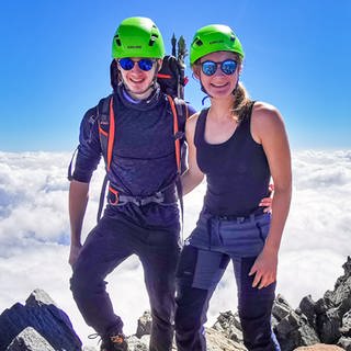 Zwanzigjähirger Frau und Mann stehen mit Wanderausrüstung auf dem Gipfel eines Berges. 