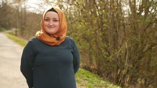 Eine junge Muslima mit orangefarbenem Kopftuch auf einem Spazierweg 