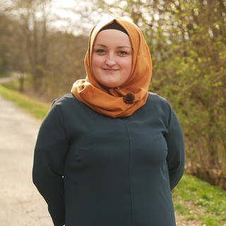 Eine junge Muslima mit orangefarbenem Kopftuch auf einem Spazierweg 