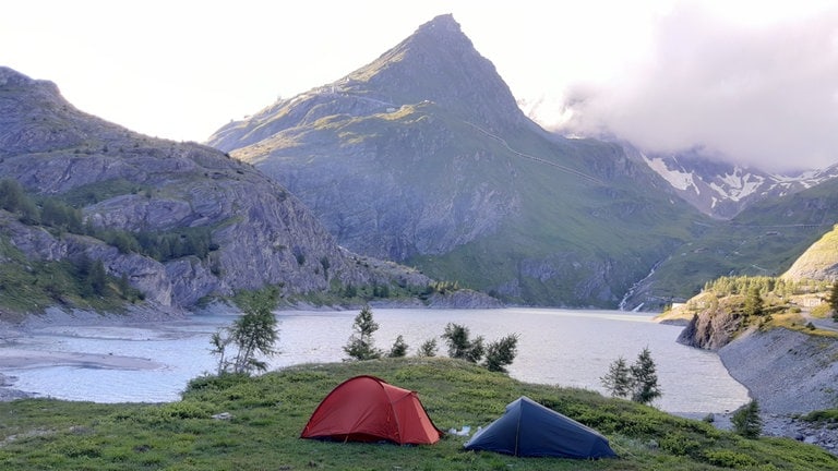 Zwei aufgebaute Zelte. Im Hintergrund sind die Alpen zu sehen.