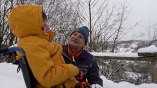 Ein Mann schaut seine Tochter an, beide sind in Winterkleidung im verschneiten Freien.