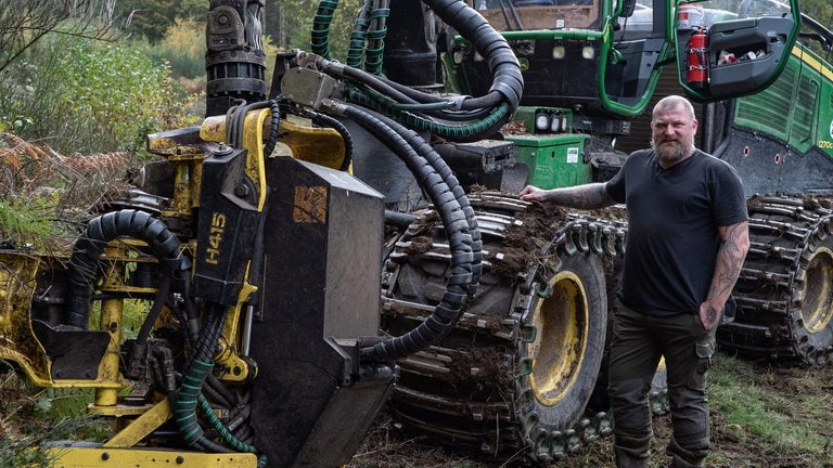 Ein Mann steht vor einem großen Harvester und hält seine Hand auf der Kette