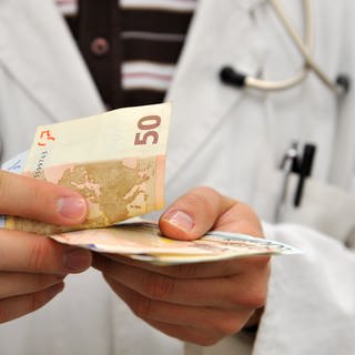 Ein Mann im Arztkittel zählt Geldscheine