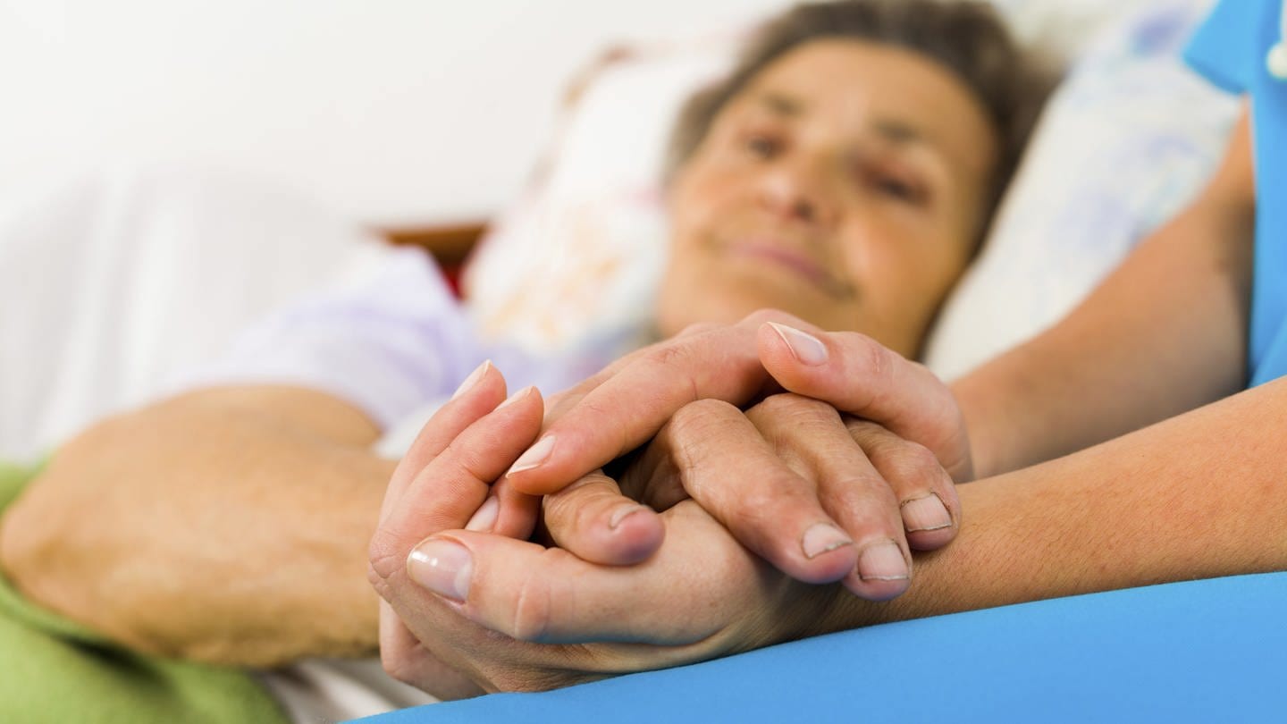Eine Krankenschwester hält die Hand einer älteren Frau