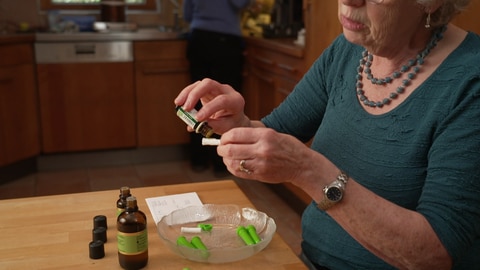 Zu sehen ist Aromaexpertin Dorothea Hamm. Sie bastelt einen Riechstift. In der Hand hält sie eine Art Docht, der sich im Rohling befindet. Darauf gibt sie einige Tropfen eines ätherischen Öls.