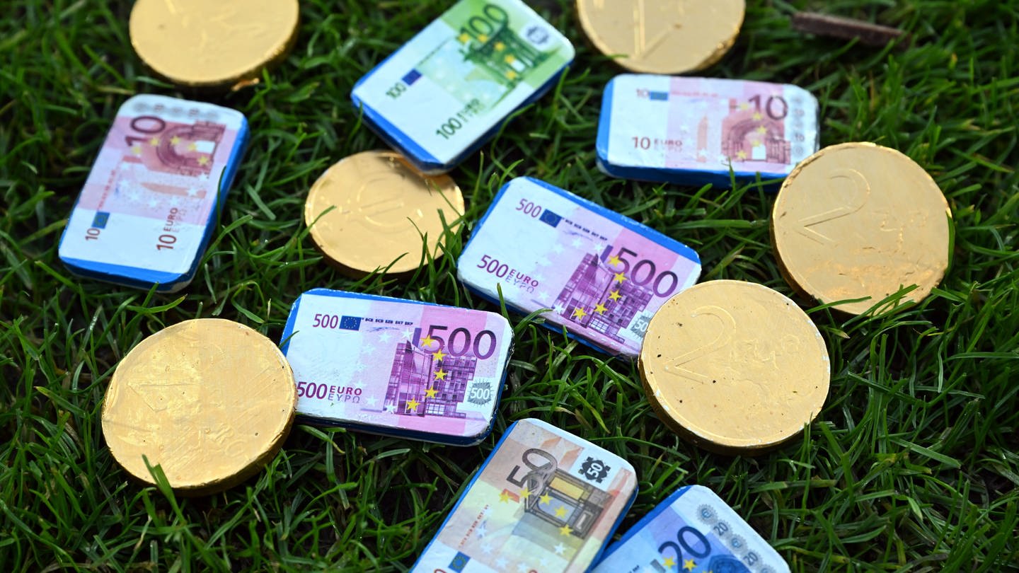 Münzen und Euro-Scheine liegen auf einem Stück Rasen. Wieviel bringt die Fußball-WM uns wirtschaflich?