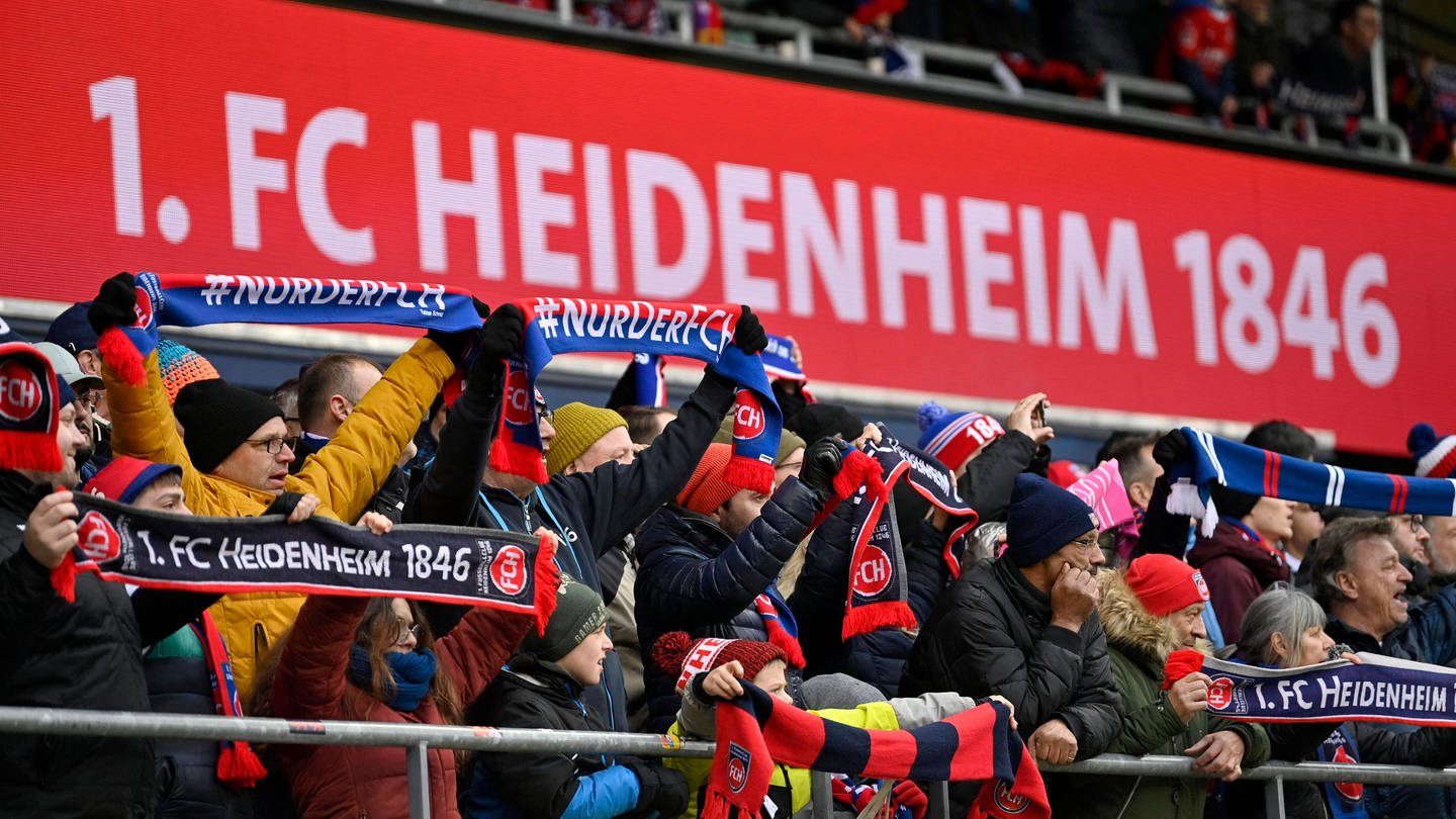 Fans des 1. FC Heidenheim mit Schals vor Schriftzug